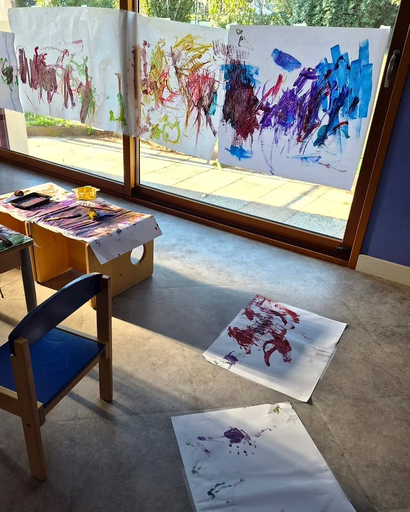 Peintures d'enfants accrochées à la baie vitrée et posées au sol pour sécher